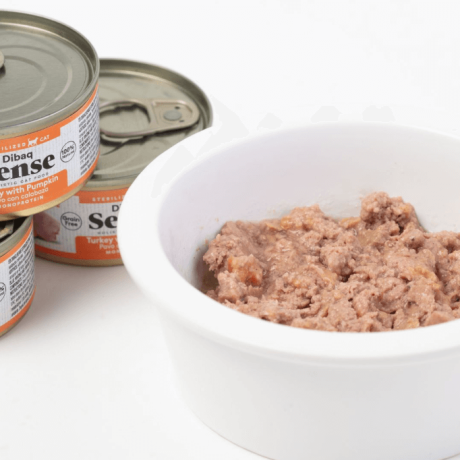 Cuenco blanco con paté de pavo y calabaza Dibaq Sense para gatos esterilizados junto a latas del producto