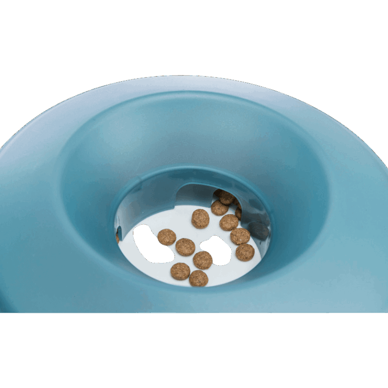 Primer plano del orificio central del comedero Trixie Rocking Bowl azul, con varias croquetas de pienso visibles en el fondo blanco. Demuestra cómo el alimento es dispensado gradualmente.