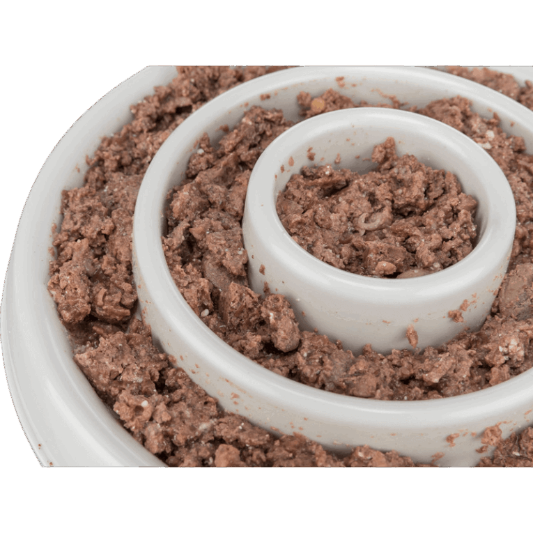 Vista de primer plano extremo del comedero slow feeding de 23cm lleno de paté de carne. El alimento húmedo se encuentra firmemente adherido a las paredes de los anillos concéntricos de plástico blanco.