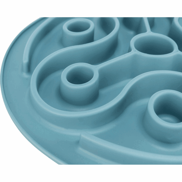 Vista lateral de cerca del mantel Slow Feeding Trixie azul de 28cm, enfocada en la profundidad y curvatura de los canales del laberinto, incluyendo varios pozos circulares vacíos.