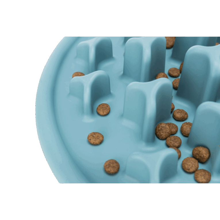 Primer plano lateral del mantel Slow Feeding Trixie de color azul, con pienso seco disperso en la base. Las croquetas se ven atrapadas entre los pilares para ralentizar la ingesta.